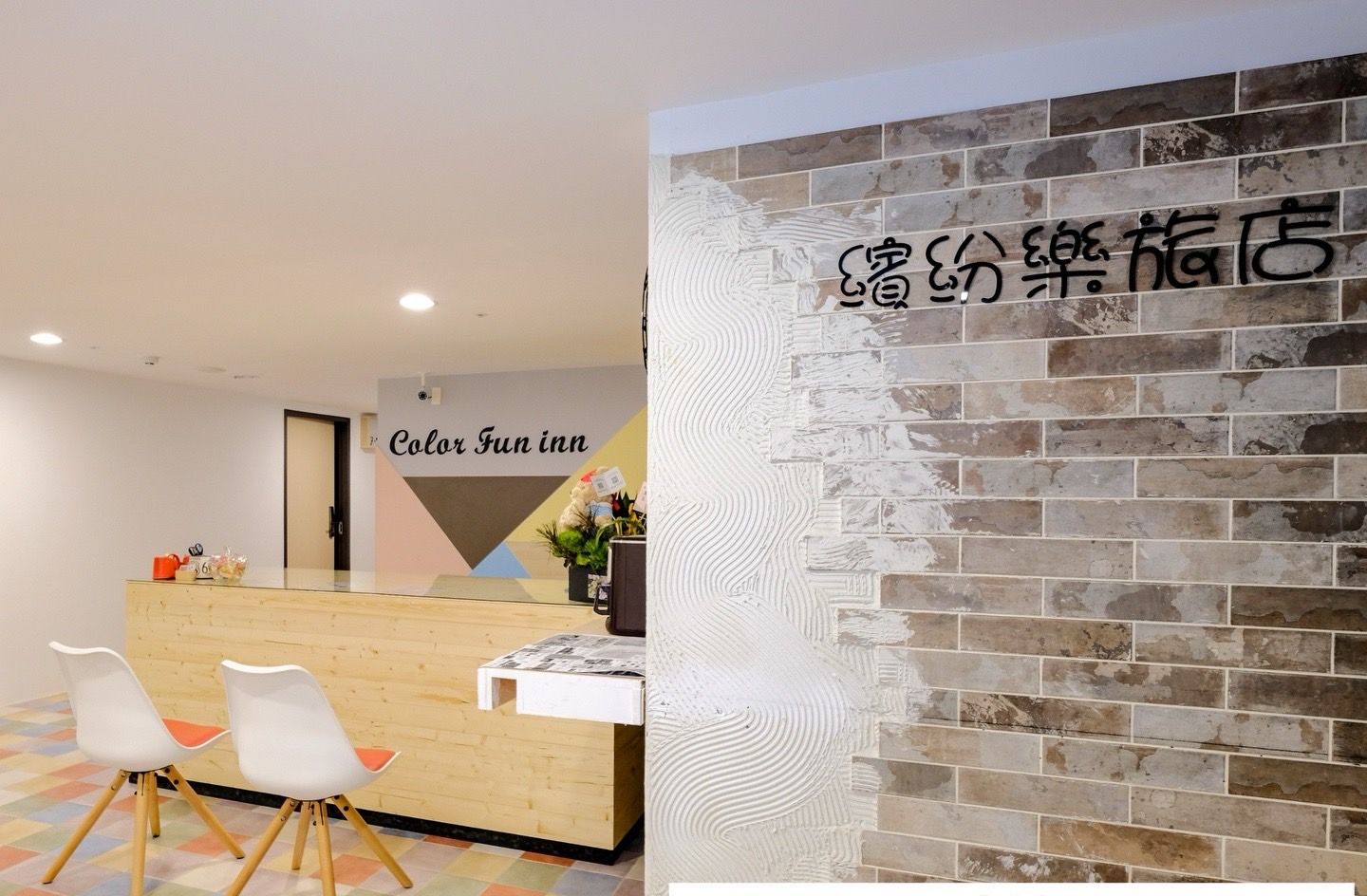 A hotel reception area with a wooden counter, white chairs, and a colorful floor. A sign reads "Color Fun inn."