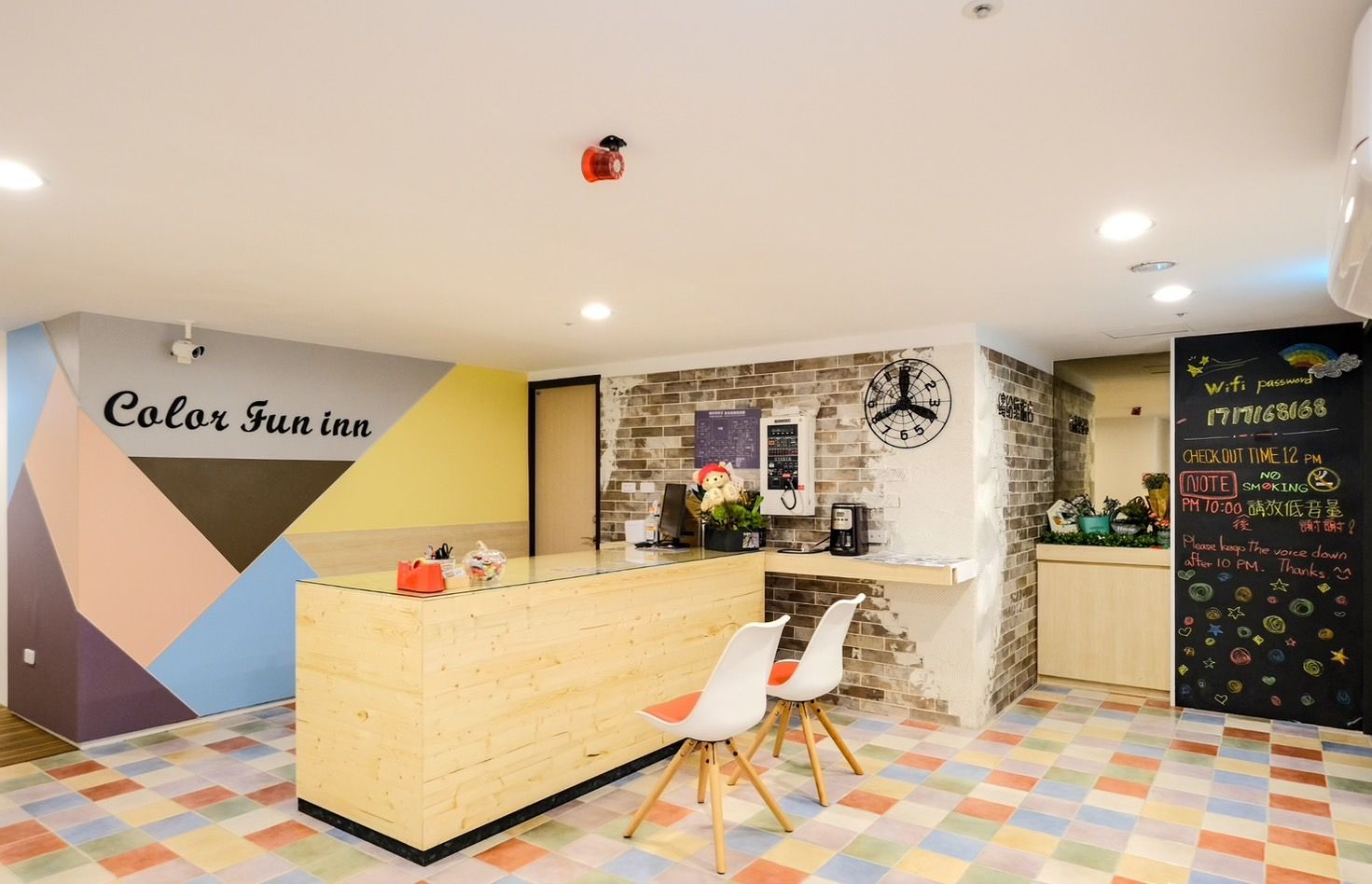 A hotel reception area with a wooden counter, a clock, and a chalkboard with check-in information.