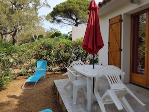 A patio with a table and chairs, surrounded by greenery and a wooden door.