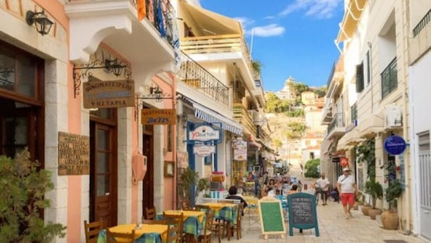 A narrow street lined with cafes and shops, featuring outdoor seating and a variety of signage. - Glyfada Villas 2 (North Kynouria)