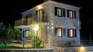 A two-story stone building with a balcony, illuminated by exterior lights. - Glyfada Villas 2 (North Kynouria)