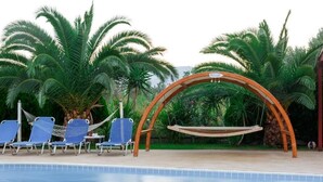 A poolside area with a hammock swing, lounge chairs, and palm trees. - Glyfada Villas 2 (North Kynouria)