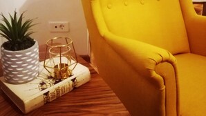 Un fauteuil jaune dans une pièce dont le sol est en bois, avec une plante en pot blanche et un livre décoratif.