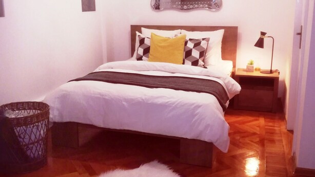 Une chambre à coucher bien rangée, avec un lit, une table de chevet, un miroir et une petite lampe.