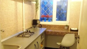Une cuisine compacte équipée d’une cuisinière à gaz, d’un évier et d’une fenêtre donnant sur un jardin fleuri.