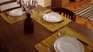 Un coin repas avec une table en bois dressée pour quatre personnes, un vase contenant des branches de coton et un téléviseur pos é sur un meuble en bois.