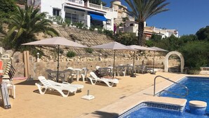 A poolside area with lounge chairs and umbrellas, a stone wall, and a clear blue pool. - Casa Jomy, a beautiful place! Sea views! (Campello)