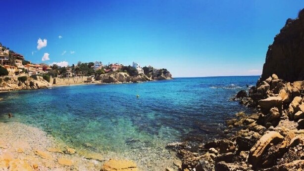 A coastal scene with clear blue water, rocky shore, and buildings on a hillside. - Casa Jomy, a beautiful place! Sea views! (Campello)