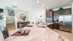 A modern kitchen with a marble countertop, stainless steel appliances, and a dining area with a table set for two. - Spacious Villa with Home Theater at Encore (Kissimmee)
