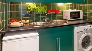 Een kleine keuken met groene kastjes, een magnetron, een spoelbak en een wasmachine.