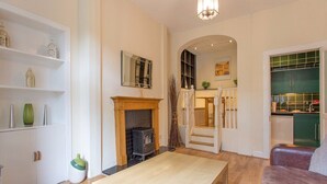 Een moderne woonkamer met een open haard, een houten tafel en een groene keuken op de achtergrond.