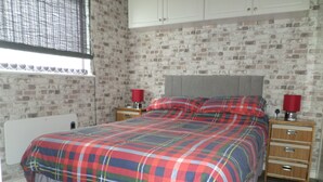 A bedroom with a plaid bedspread, wooden nightstands, a white radiator, and a brick-patterned wall. - Chalet Lighthouse, Kessingland (Kessingland)