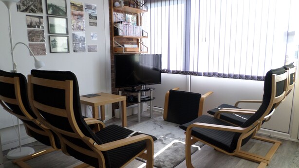 A living room with two wooden chairs, a small table, a TV, and a bookshelf. - Chalet Lighthouse, Kessingland (Kessingland)