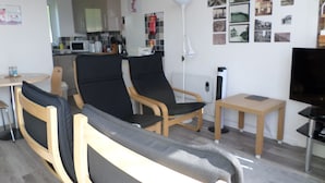 A living room with a sofa, two black chairs, a small table, a TV, and a kitchen in the background. - Chalet Lighthouse, Kessingland (Kessingland)