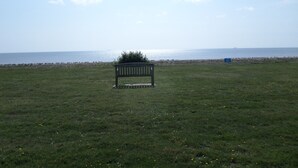 A grassy field with a bench and a distant view of the sea. - Chalet Lighthouse, Kessingland (Kessingland)