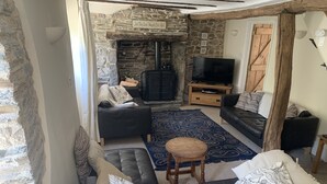 Una sala de estar acogedora con chimenea de piedra, un sofá de cuero negro, una mesa de centro de madera y un televisor.