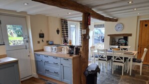 Una cocina con piso de piedra, techo de vigas de madera y un comedor con sillas blancas.