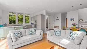 A modern living room with two grey sofas, a wooden coffee table, and a kitchen area with a central island. - Beautiful holiday home, just a walk away from Talland beach... (Looe)