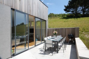 Een modern huis met een patio, compleet met een eettafel voor zes personen, een barbecue en een grote schuifdeur die leidt naar de binnenruimte.