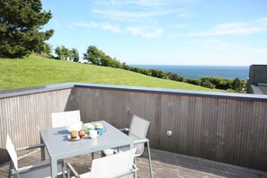 Een terras met een tafel en stoelen, een houten omheining en uitzicht op zee.