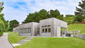 A modern two-story building with a wooden exterior, large windows, and a staircase leading to the entrance. - Beautiful holiday home, just a walk away from Talland beach... (Looe)