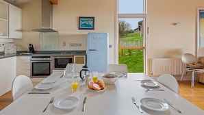 Une cuisine moderne avec une grande fenêtre, une table à manger dressée pour le petit-déjeuner et une vue sur un jardin.