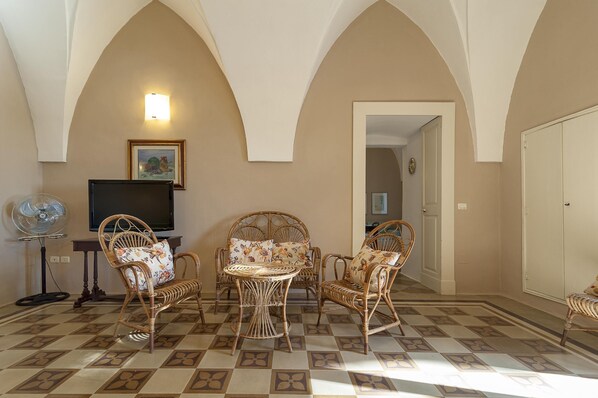 A room with a checkered floor, wicker furniture, a flat-screen TV, and a fan.