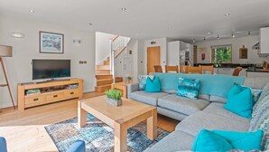 A modern living room with a grey sofa, a wooden coffee table, and a TV on a wooden stand. A staircase leads to the upper floor. - This fantastic pet friendly,  contemporary property features a south-west facing balcony off the mas (Looe)