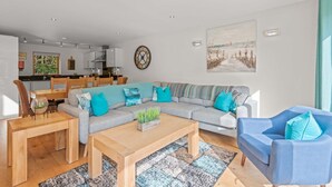 A modern living room with a grey sofa, blue armchairs, and a wooden coffee table. A dining area with a wooden table and chairs is visible in the background. - This fantastic pet friendly,  contemporary property features a south-west facing balcony off the mas (Looe)