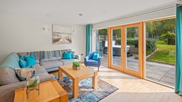 A modern living room with a grey sofa, blue armchairs, and a wooden coffee table. There is a painting on the wall and a glass door leading to a garden. - This fantastic pet friendly,  contemporary property features a south-west facing balcony off the mas (Looe)