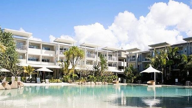 Un resort con piscina rodeada de palmeras y sillas de descanso.