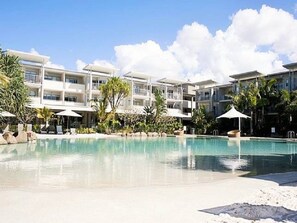Un complexe hôtelier doté d’une piscine entourée de palmiers et de chaises longues.