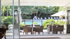 Un área de estar exterior con mobiliario de mimbre, piscina y plantas tropicales.