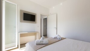 Una camera d'hotel con un letto, una TV a parete, una scrivania e una porta che conduce al bagno.