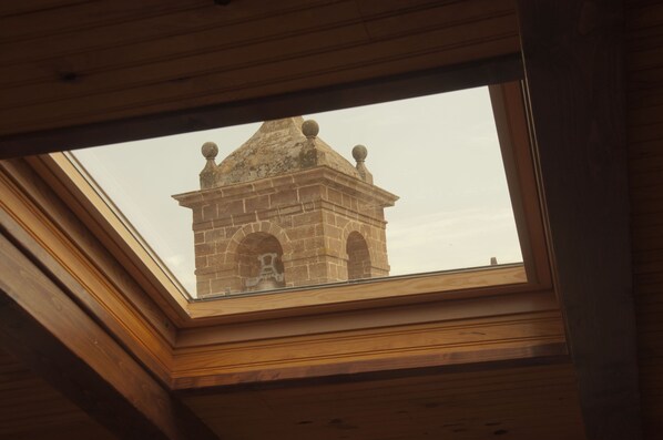 Un tragaluz con vista a una torre de piedra con ventanas de arco y techo puntiagudo.