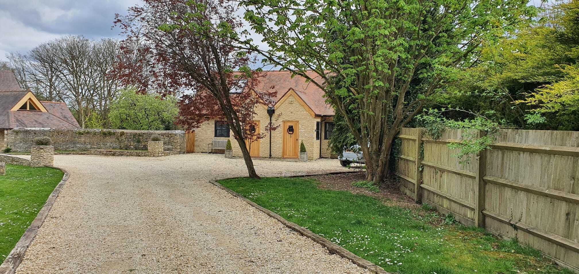 Une maison avec une allée en gravier menant à une porte en bois, entourée d’un mur de pierre et d’une clôture en bois.