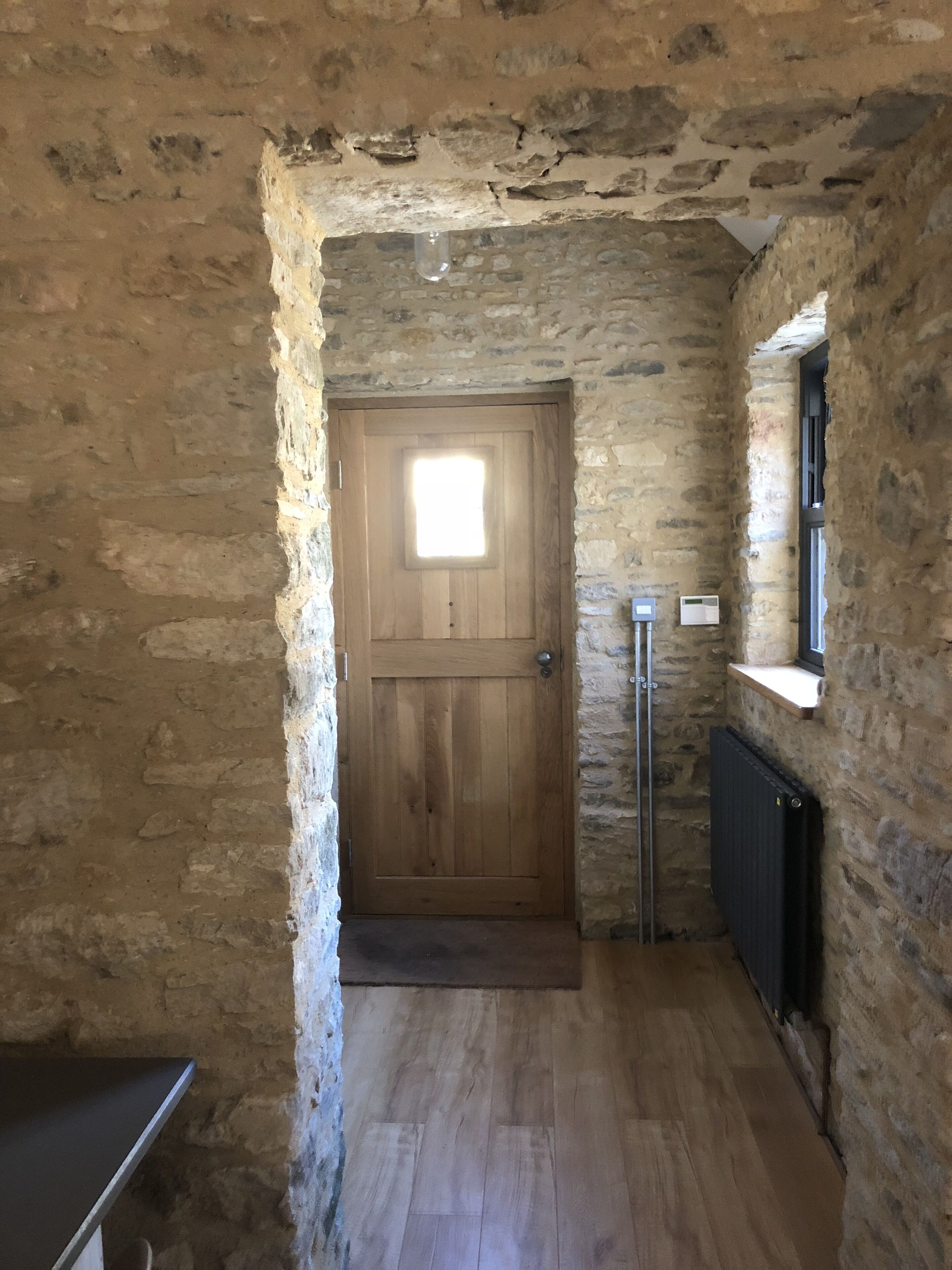 Un corridoio con pareti in pietra, una porta in legno e un termosifone.