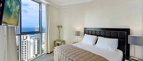 A hotel room with a large window, a bed with a headboard, a nightstand, a lamp, and a vase with flowers.