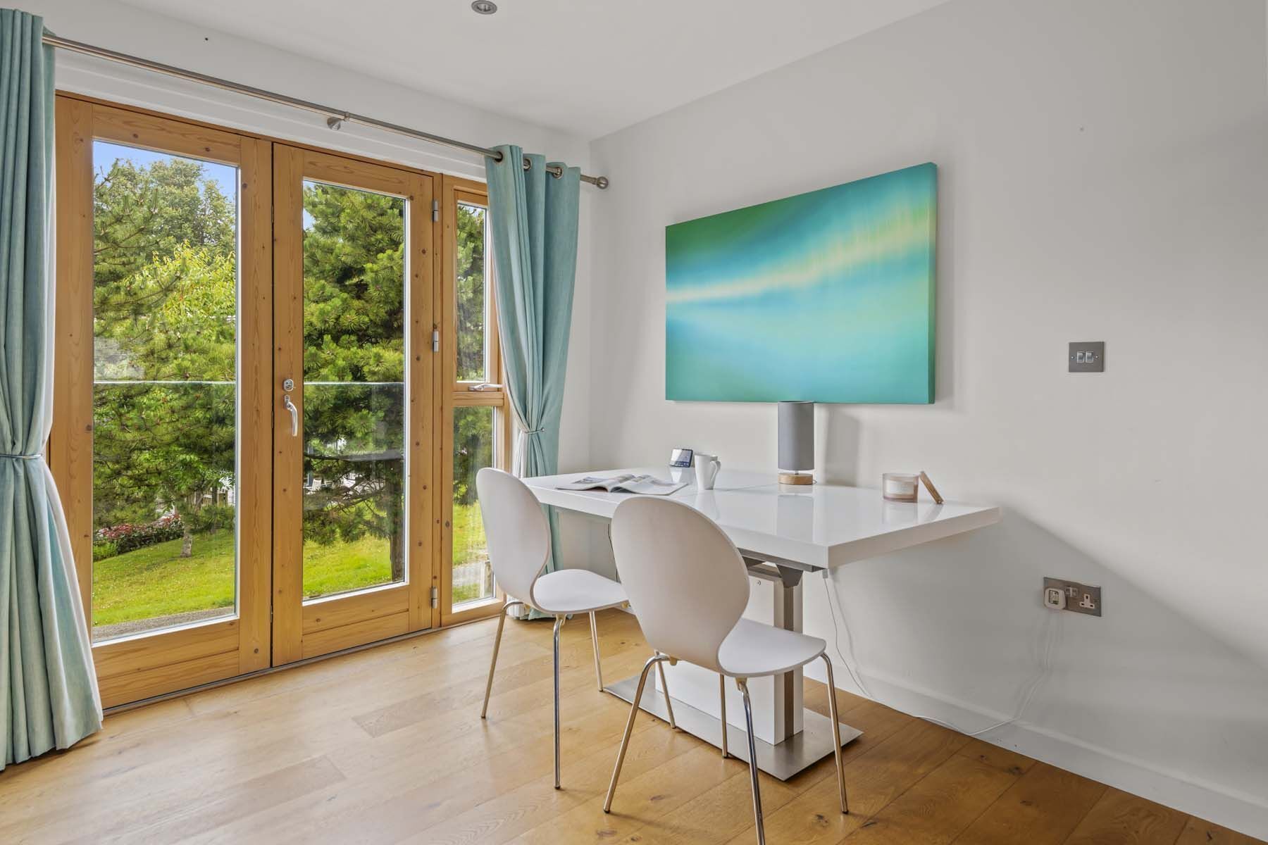 A modern dining area with a white table, two white chairs, and a large abstract painting on the wall.