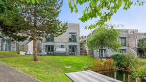 Ein modernes, zweistöckiges Haus mit Steinaußenwand, einer Holzterrasse und einem kleinen Teich.