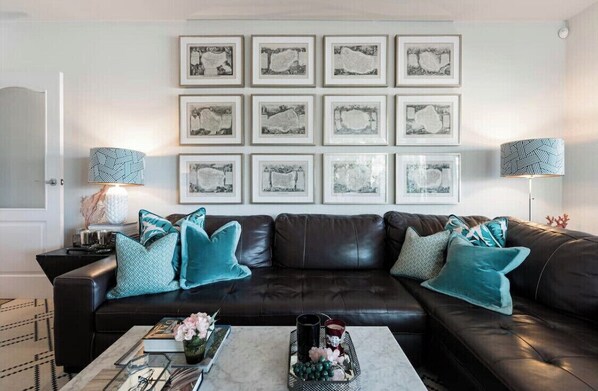A living room with a dark leather sofa, teal cushions, a coffee table with decorative items, and framed artwork on the wall. - SEA, GOLF, RELAX, LANDSCAPE, POOL (Rincón de la Victoria)