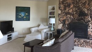 A living room with a stone fireplace, a television, a bookshelf, and a painting. - Big and Bright,  Steps to Sand, Ocean Views, and Sleeps 8+ (La Selva Beach)