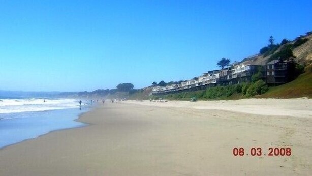 A beach with a clear sky, a sandy shore, and houses along the coastline. - Big and Bright,  Steps to Sand, Ocean Views, and Sleeps 8+ (La Selva Beach)