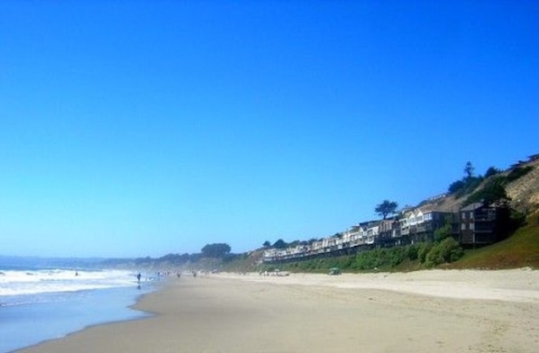 A beach with a clear sky, a sandy shore, and houses along the coastline. - Big and Bright, Steps to Sand, Ocean Views, and Sleeps 8+ (La Selva Beach)