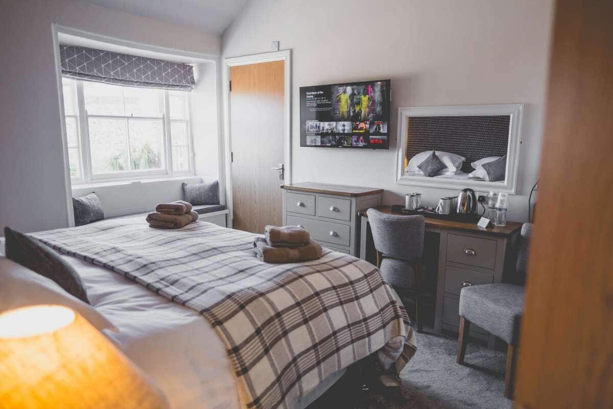 A bedroom with a bed, a desk, a chair, a TV, and a window.
