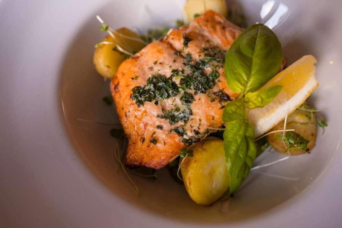 A plate with a piece of salmon, lemon slices, and greens.