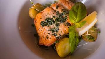 A plate with a piece of salmon, lemon slices, and greens.