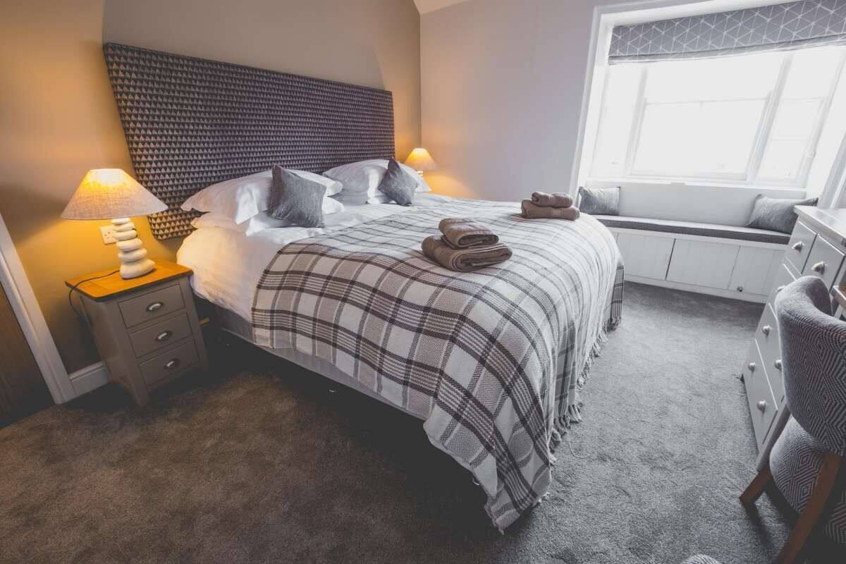A neatly made bed with a plaid bedspread, a bedside lamp, and a window seat with cushions.