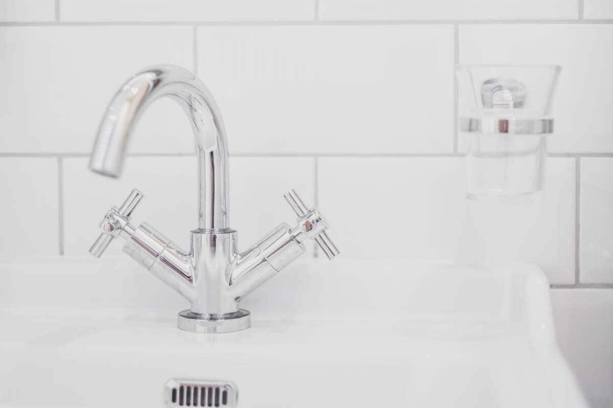 Ein chromfarbener Wasserhahn mit mehreren Armaturen, eine weiß geflieste Wand und eine klare Glas-Seifenspender.