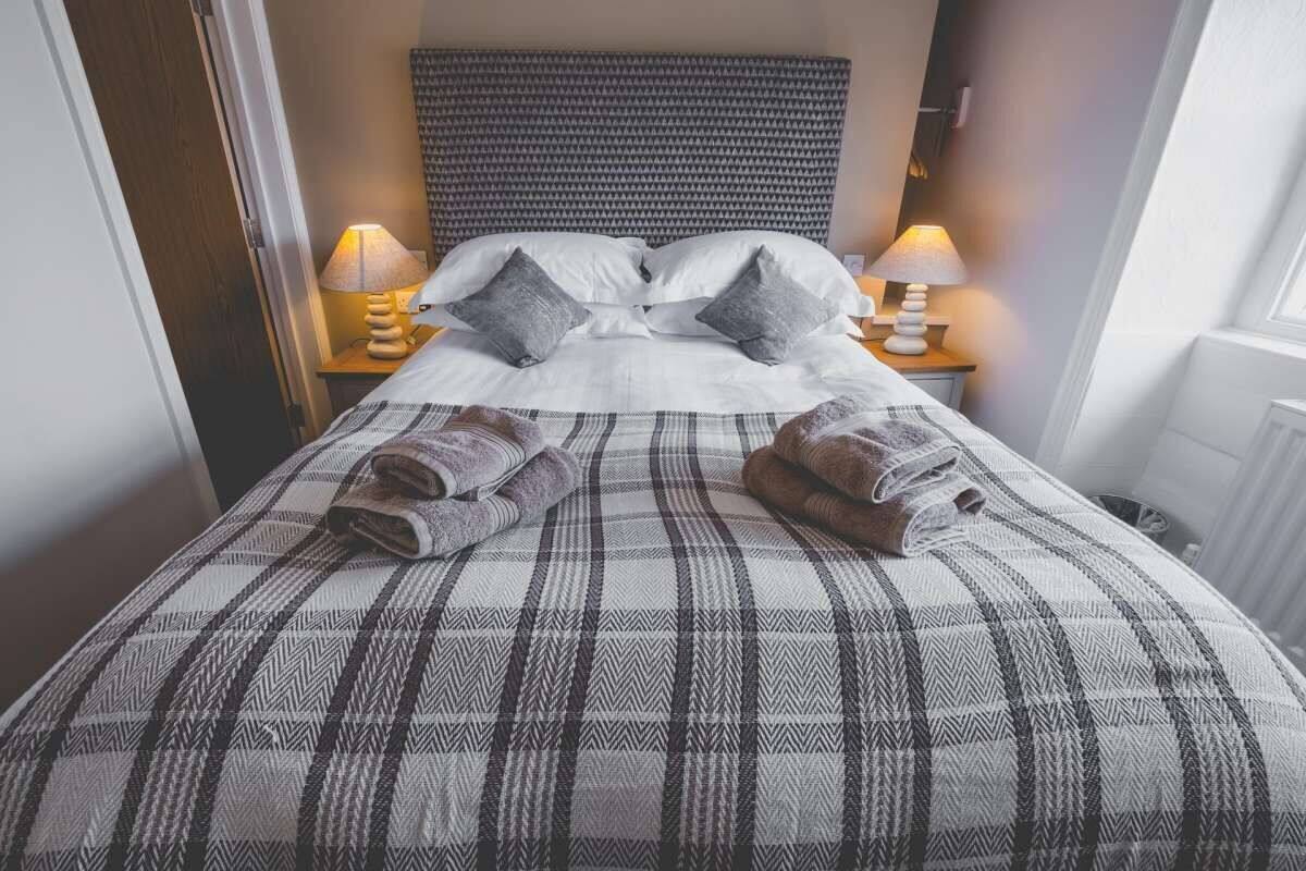 A neatly made bed with a plaid bedspread, two pillows, and two rolled towels.